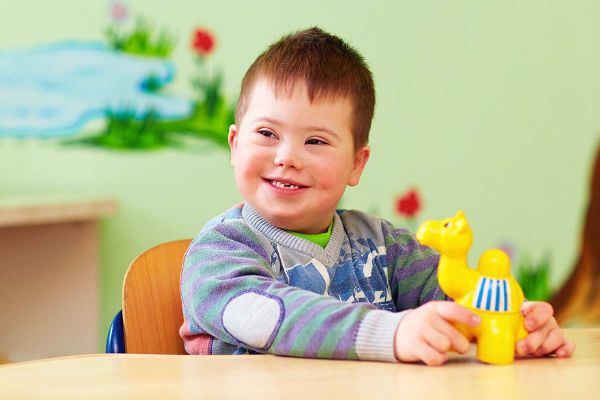 A special needs child smiles and plays with a yellow toy